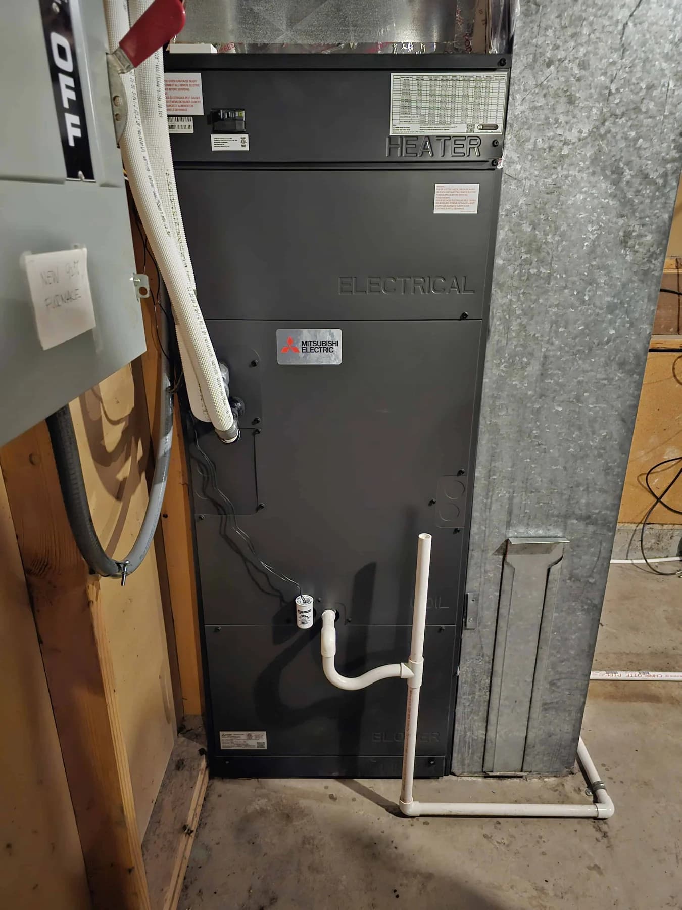 Indoor Mitsubishi Electric air handler beside ductwork, with equipment labels and drain piping visible